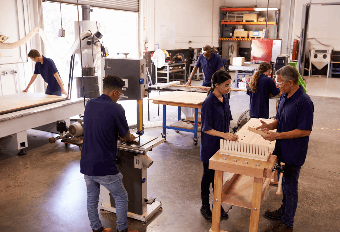 A diverse group of apprentices and instructors working together in a woodworking workshop, using machinery and hand tools to build practical skills, representing hands-on learning, mentoring and lifelong skills development during National Apprenticeship Week 2026.