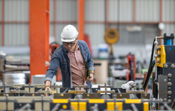 A manufacturing operative inspects a production line and adjusts components, demonstrating lean manufacturing practices focused on process efficiency, quality control, and waste reduction through skilled operational training.