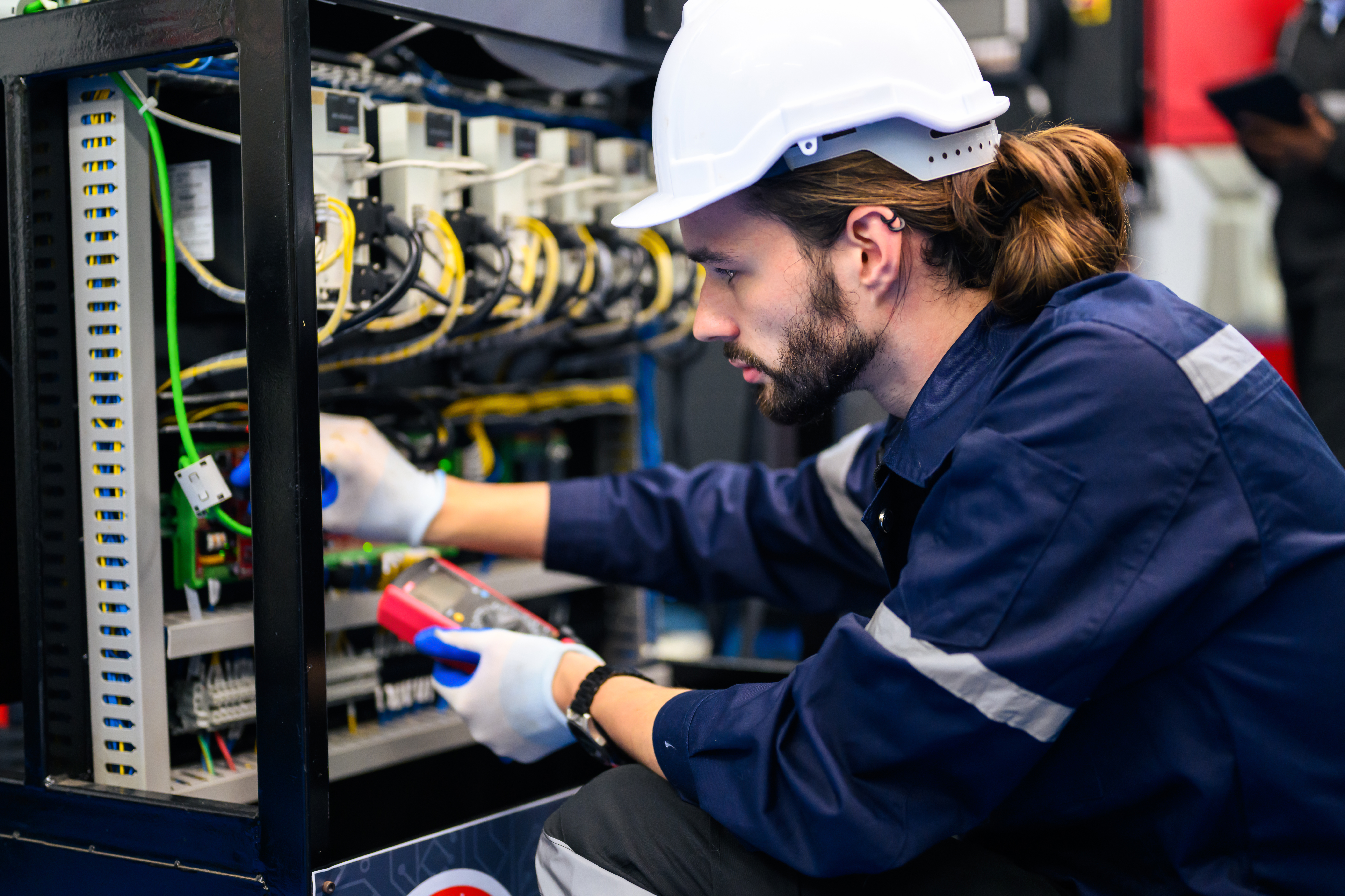 Mechatronics Maintenance Technician Apprenticeship training with a technician inspecting electrical equipment and industrial wiring.