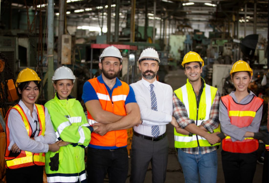 A diverse team stands together with confidence in a manufacturing plant, showcasing the successful execution of an apprenticeship levy management plan.