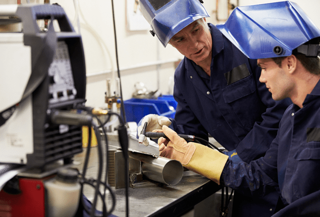 An apprentice welder follows the instructions given by a skilled engineer.